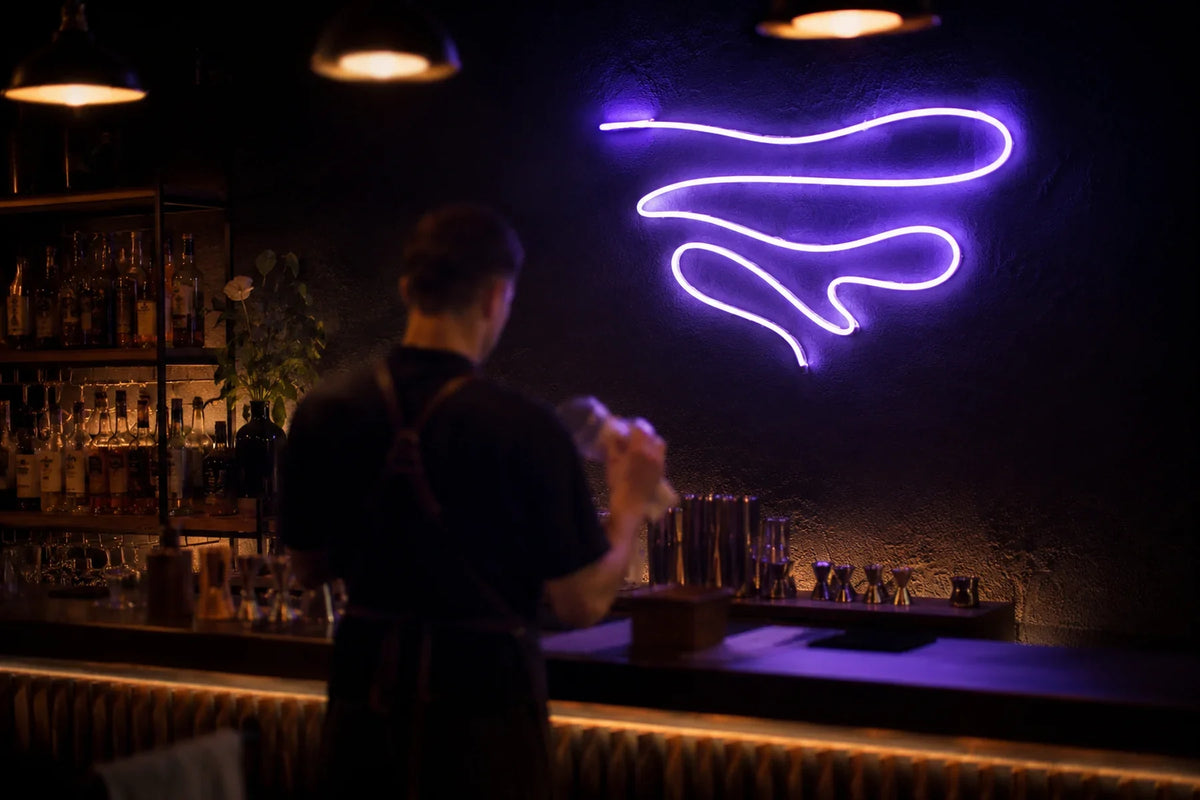 Enseigne néon LED violette allumée sur le mur d'un bar à cocktails, barman de dos
